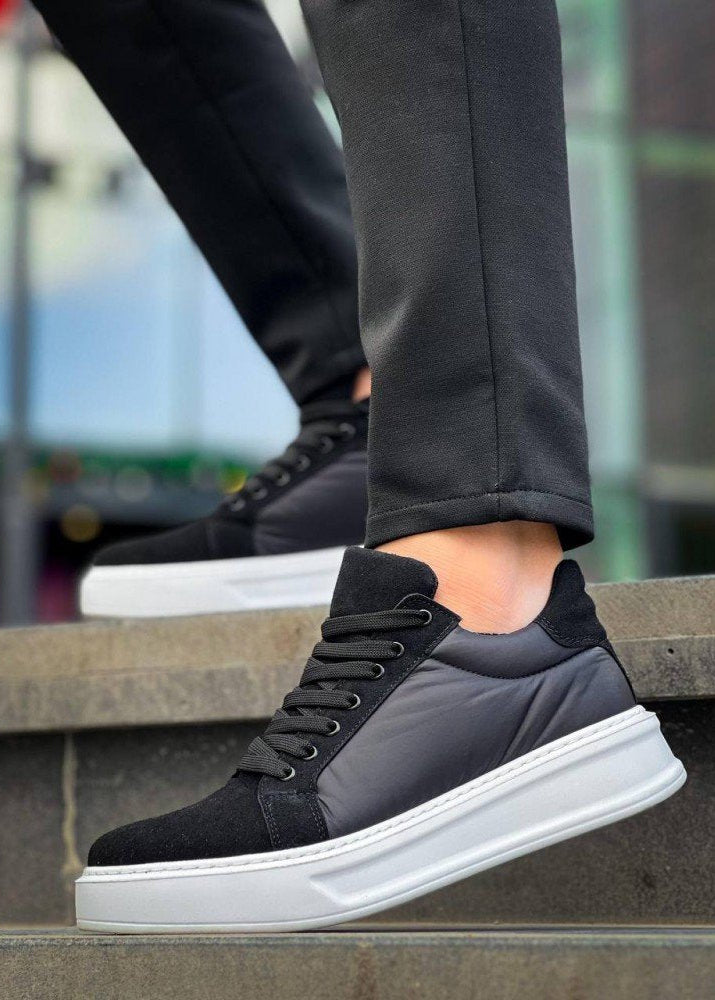 Black and gray sneaker with white sole worn by a person sitting on a concrete bench.
