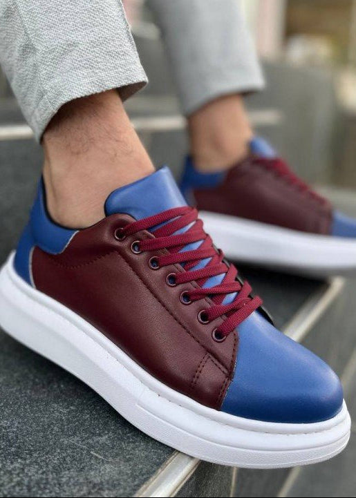 Blue and brown sneakers with white soles worn by a person sitting on a bench.