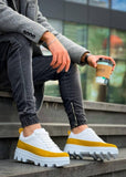 Person wearing white sneakers with yellow stripes sitting on steps holding a coffee cup.