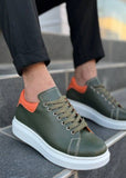 Green sneakers with orange accents worn by a person on a tiled step.