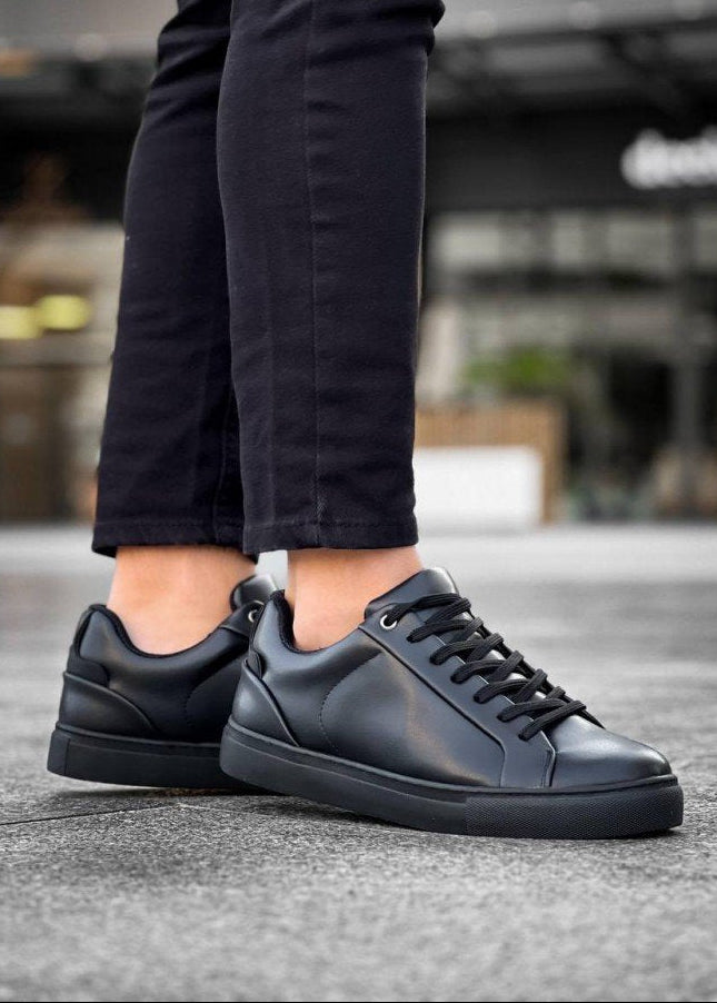 Black sneakers worn with dark pants on a blurred background