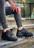 Black platform sneakers worn on a concrete surface with a blurred background