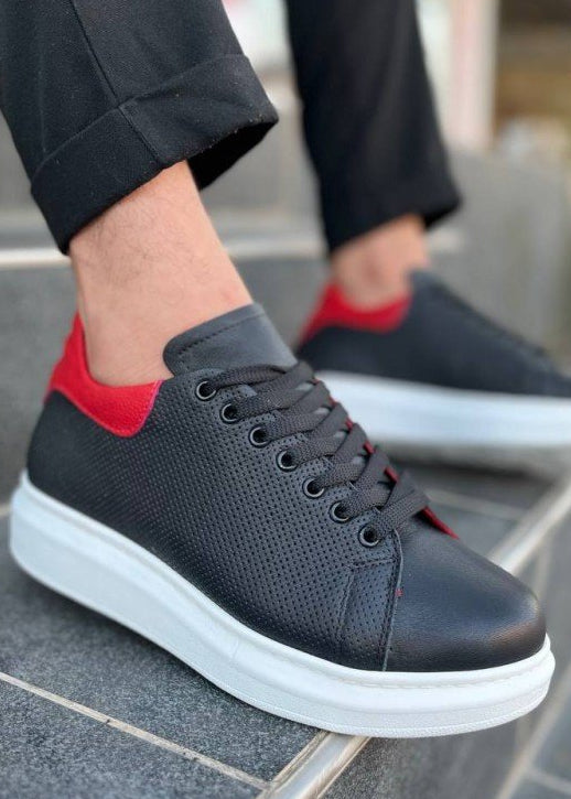 Black sneakers with red accents worn by a person on outdoor steps.