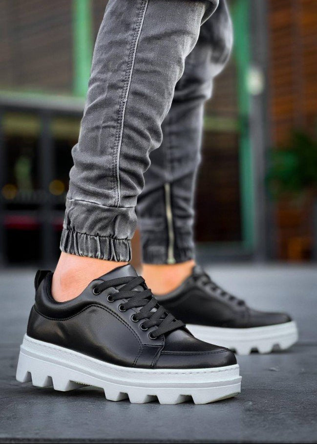 Black sneakers with white soles worn by a person on a blurred background