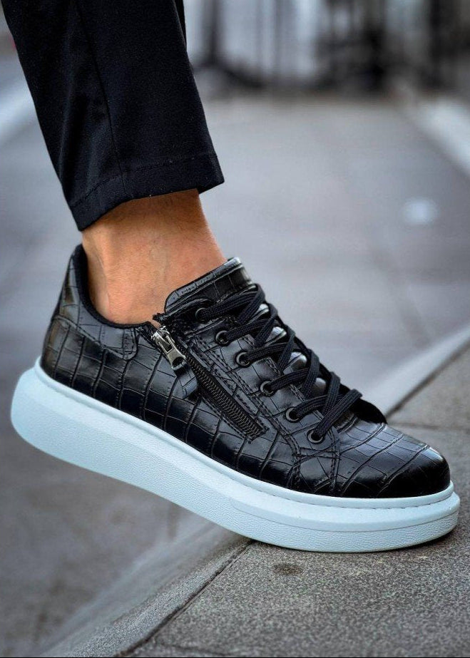 Black crocodile-patterned sneaker with a white sole on a blurred pavement background