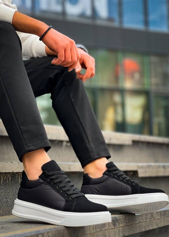 Black sneakers with white soles worn by a person sitting on steps.