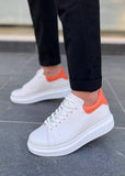 White sneakers with orange accents worn on a gray pavement.
