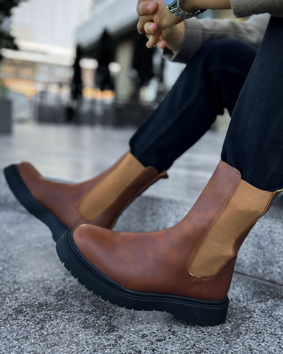 Person wearing brown leather boots with a blurred urban background